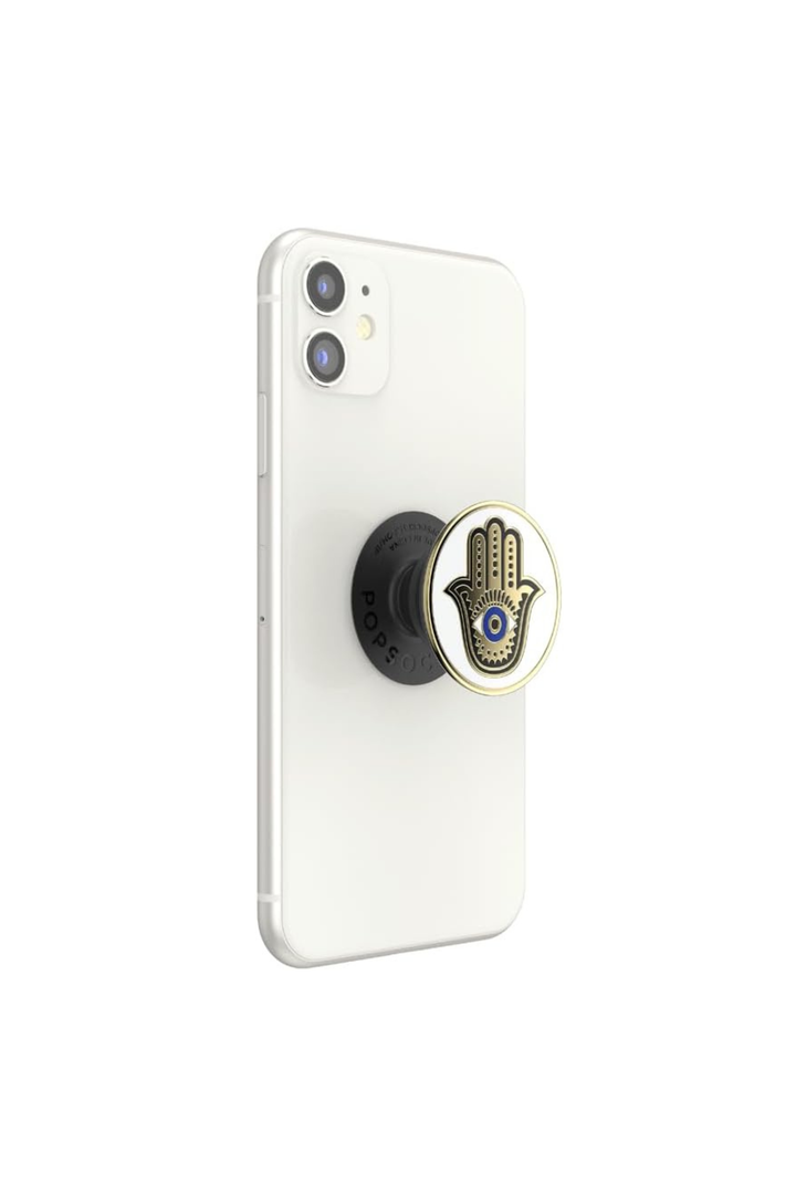A white smartphone shown from the back with a black circular pop socket attached. The pop socket has a gold-tone rim and a Hamsa hand design with a blue eye motif in the center.