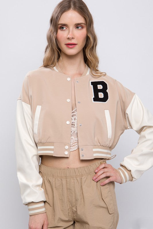 model is wearing a lace up under the Khaki Varsity Crop Jacket with beige parachute pants 