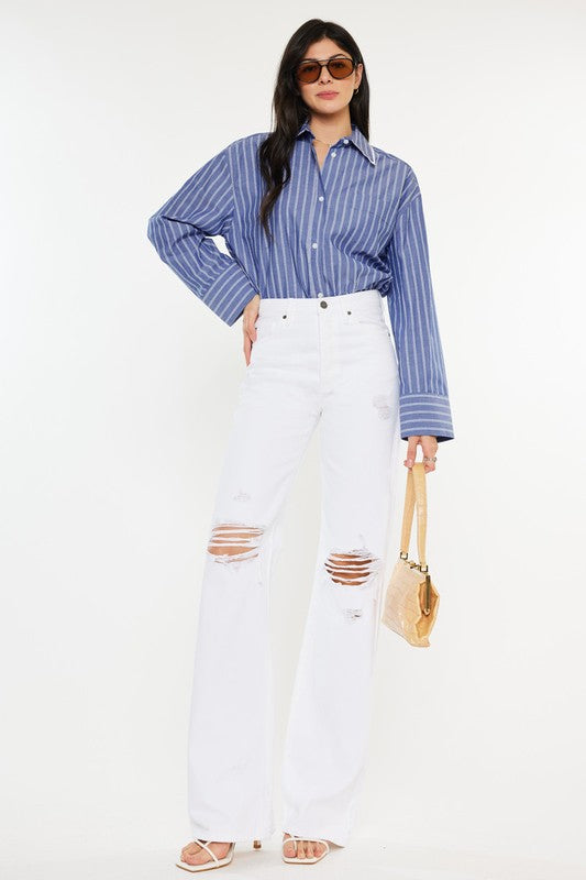 Model is wearing White High Rise Flare Jeans with white heels and a blue stripped shirt, the model is also wearing chic sunglasses and a mustard yellow handbag 