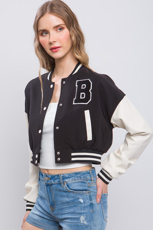 model is wearing a white top with the Black Varsity Crop Jacket and denim shorts