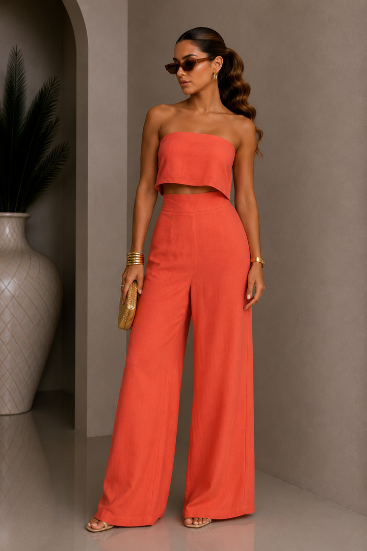 Woman in a red outfit standing against a neutral wall with a vase in the background. Orange Coral Strapless Linen Pants Set.