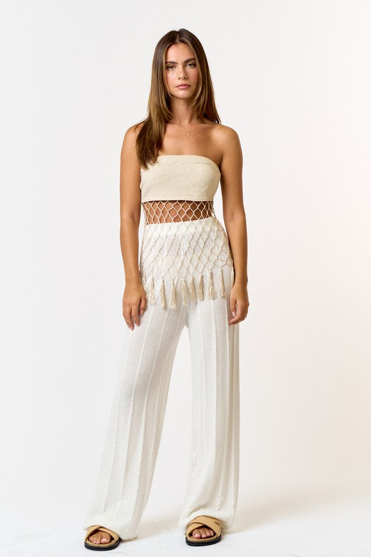 Model is wearing Natural Crochet Tassel Tube Top with white pants and beige slide sandals 