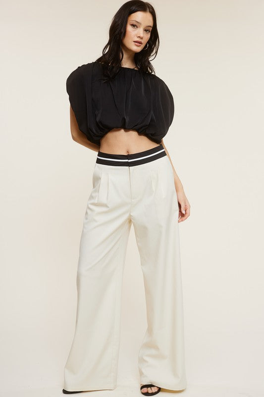Full view of the model wearing a black blouse and the Cream Talbot Trousers with black heels 