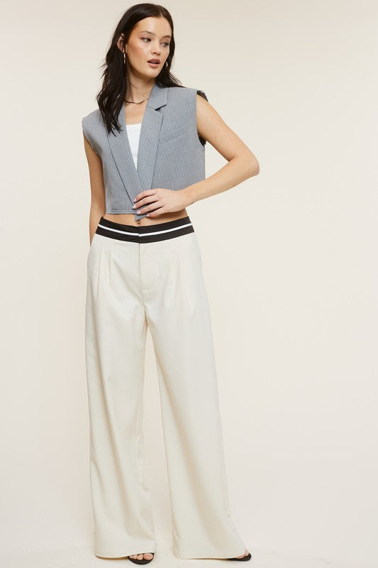 Model is wearing Cream Talbot Trousers with a vest  and gold jewelry and black heels 