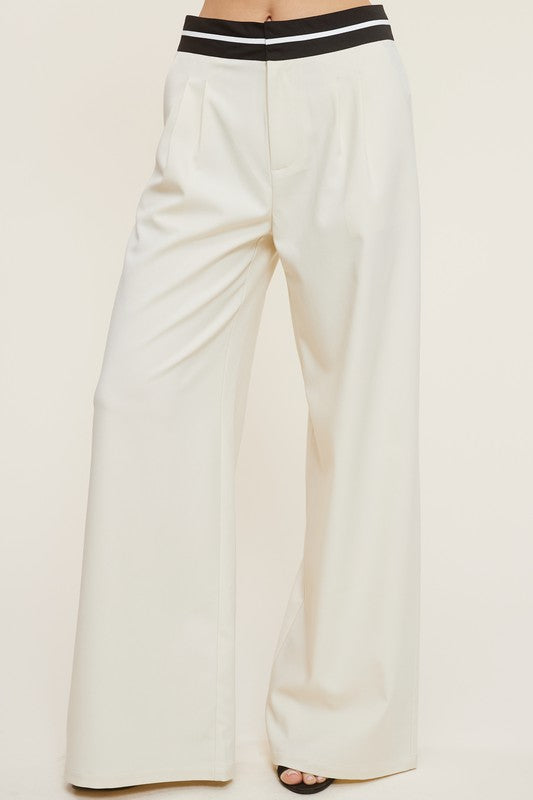 Model is wearing cream Talbot Trousers and black heels, close view of the trousers and waistband detail 