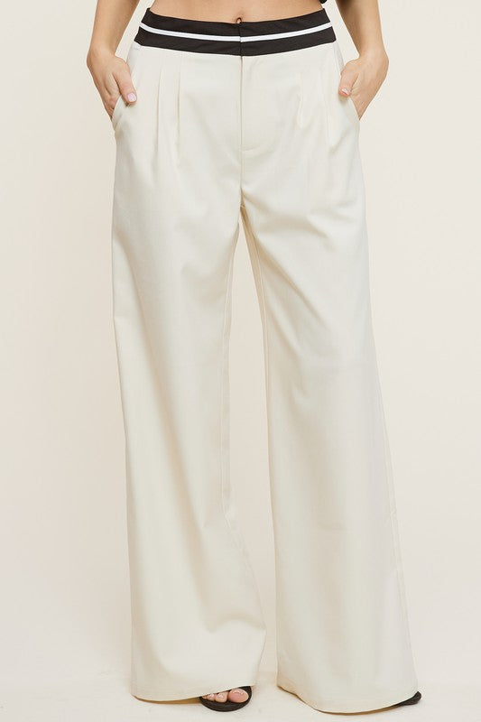 Model is wearing Cream Talbot Trousers with a waist band on black and white and black heels 