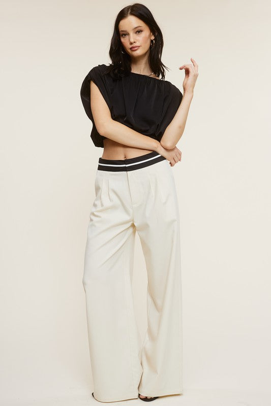 Model is wearing Cream Talbot Trousers contrast waistband and a black blouse and gold hoop earirings 