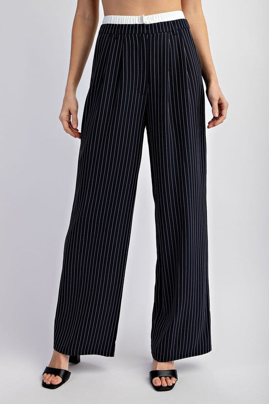 Model is wearing Navy Pinstriped Tailored Trousers and black heels, close view of the pants showing the white elastic waist hem 