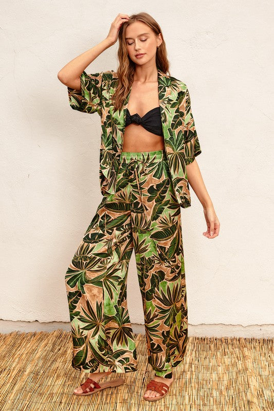 Model is wearing Green Tropical Ibiza Pull On Pants with a black bralette top and matching tropical short sleeve shirt and brown slide sandals