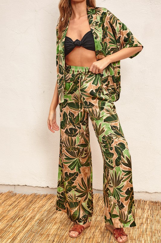 Model is wearing Green Tropical Ibiza Pull On Pants with a black bralette top and matching tropical shirt with brown sandals 