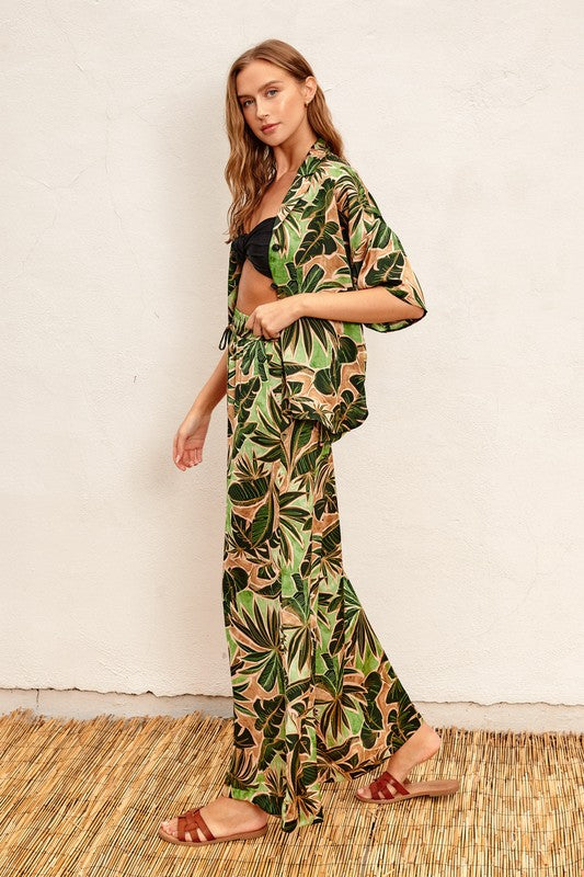 Model is wearing Green Tropical Ibiza Pull On Pants with a black bralette top and matching tropical shirt with brown sandals, side view of the outfit 