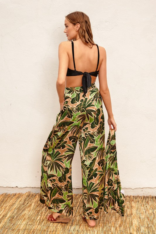 model is wearing Green Tropical Ibiza Pull On Pants with a black bralette tie back top and brown slide sandals, back view 