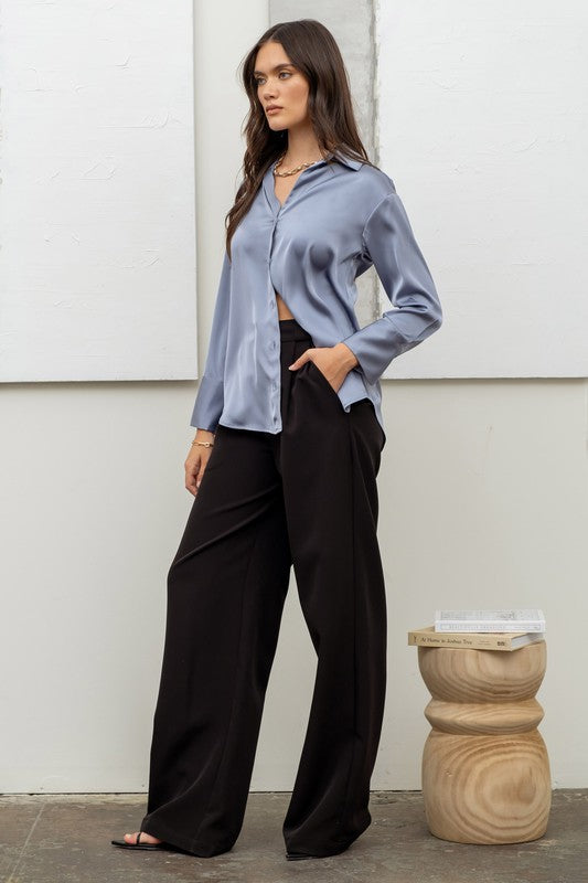 side of the model wearing Dusty Blue Satin Button Up Top with black satin pants and black high heels 