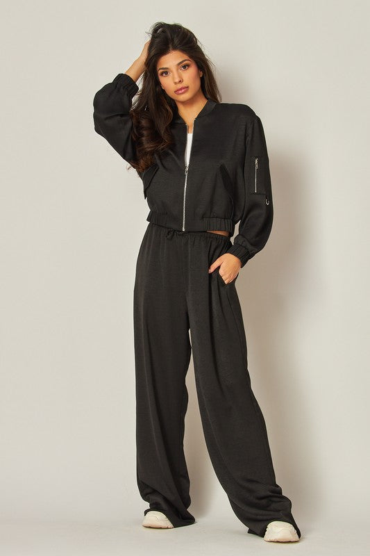 model is wearing Black Satin Bomber Jacket with a white top under the jacket, matching black wide leg pants and white sneakers