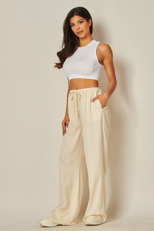 model is wearing Ivory Satin Wide Leg Pants and white top and beige sneakers 