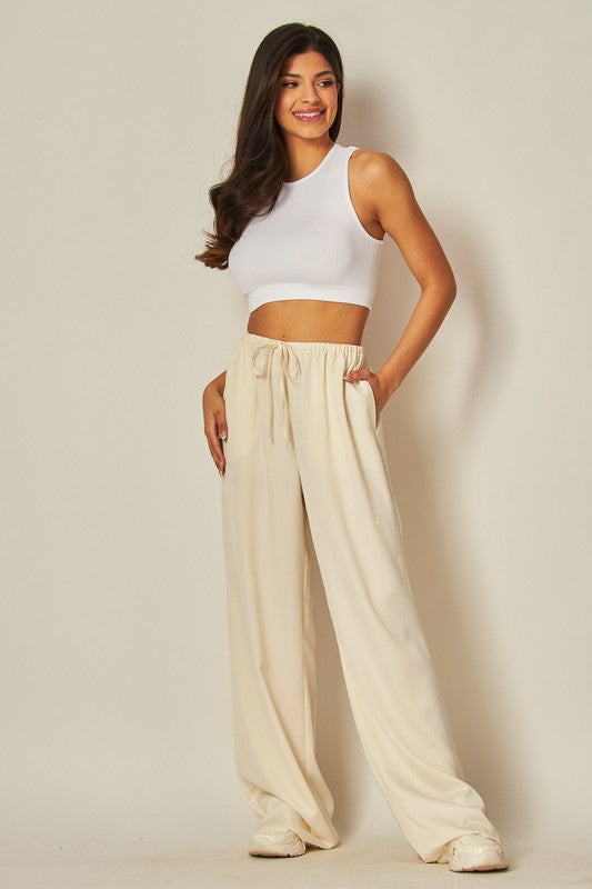 Model is wearing Ivory Satin Wide Leg Pants  and white top and sneakers 