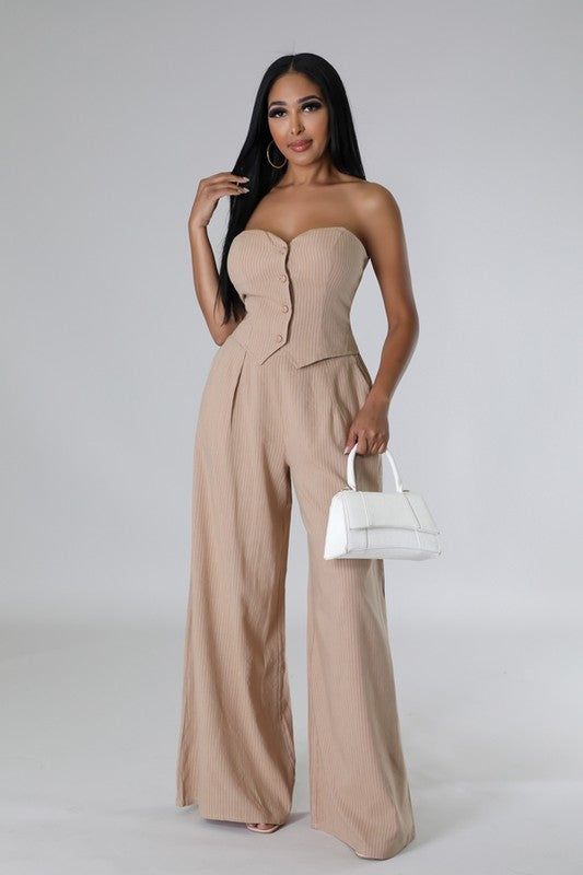 Model is wearing Taupe Stretch Pant Set with gold hoop earrings and a white mini handbag with high heels 