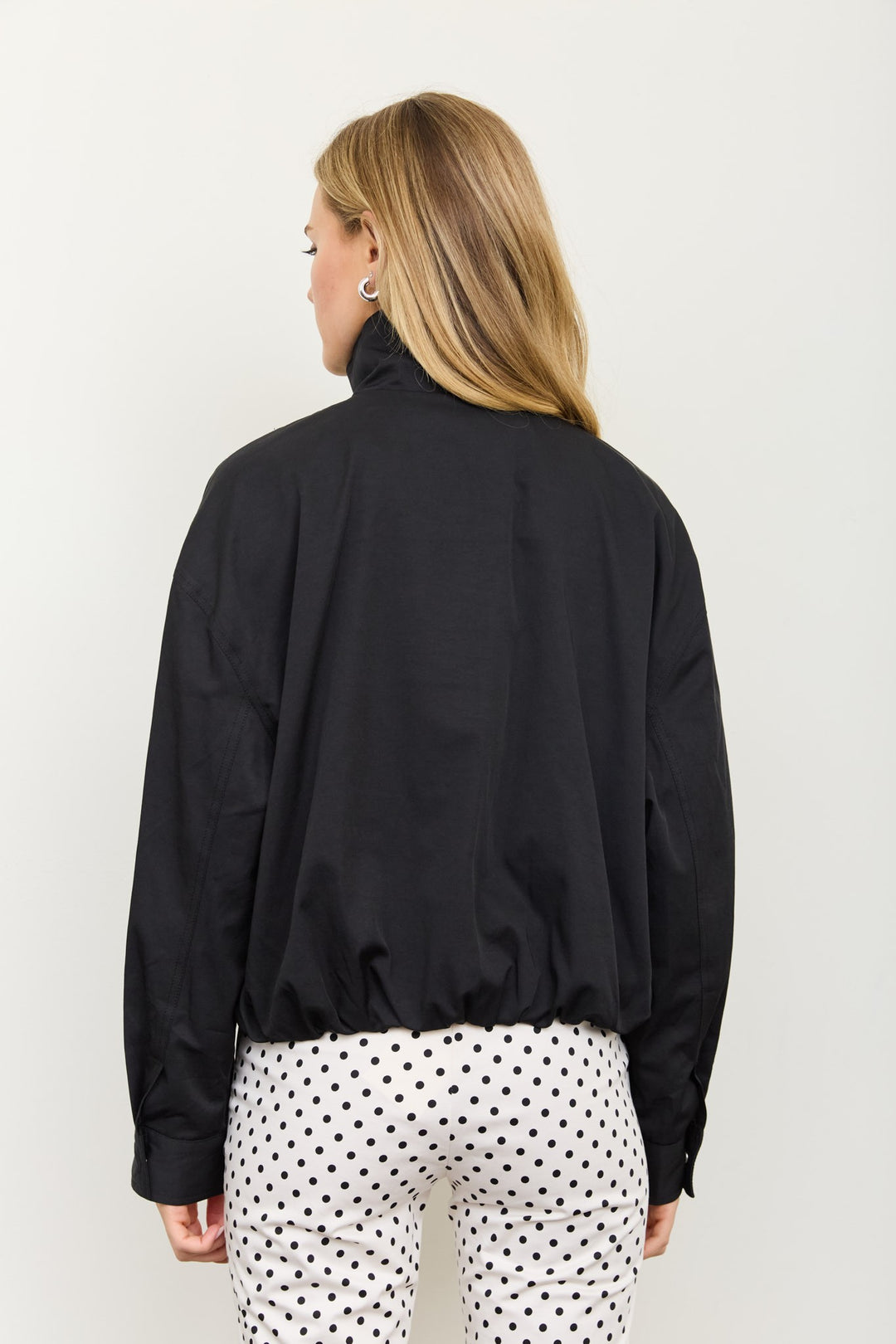 Back view of the black mock neck zip jacket with elastic cinched hem and polka dot pants