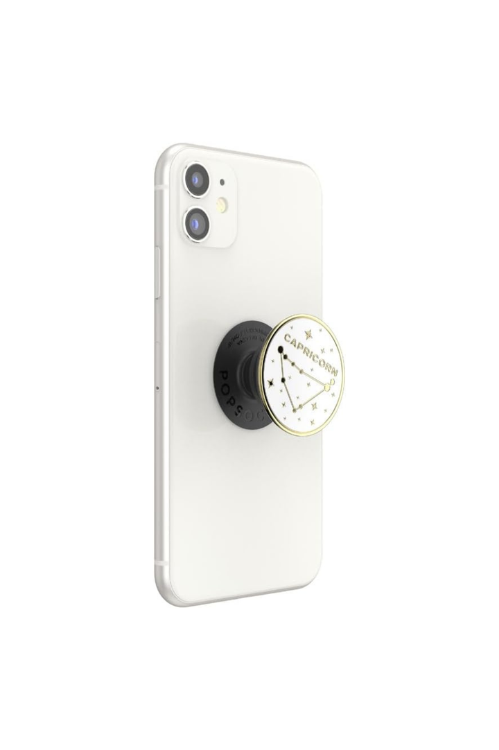 A white smartphone shown from the back with a black pop socket attached near the lower center. The pop socket has a circular dial with a gold-toned rim and a white face featuring black markings and the visible brand text &