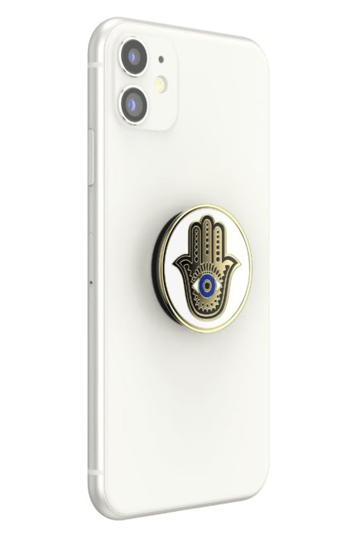 A white smartphone case with a circular pop socket on the back featuring a gold and black hamsa hand design with a blue evil eye detail, shown on a white background.