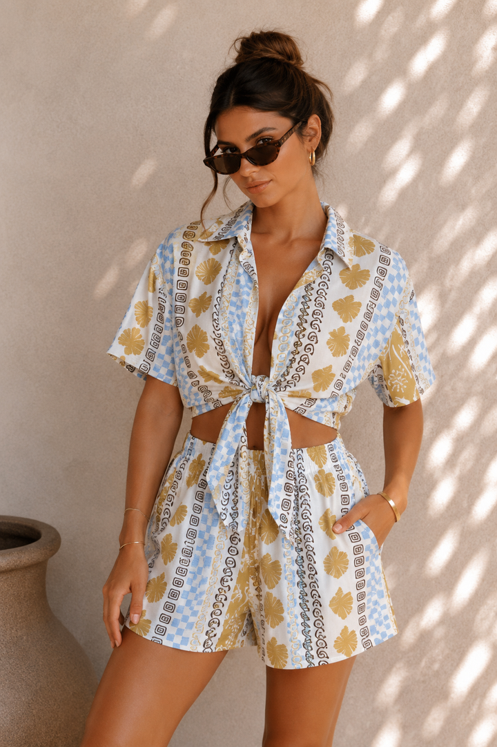 Woman wearing a patterned romper against a neutral wall.