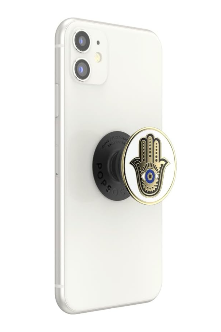 A white smartphone shown from the back with a black PopSockets grip attached. The grip has a circular gold-and-white hamsa hand design with a blue eye motif. Evil Eye Hamsa Hand White &amp; Gold Phone Grip