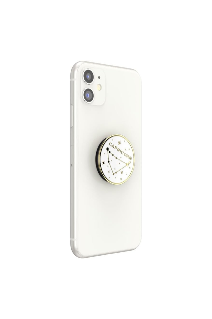 A white smartphone shown from the back with a round pop socket attached near the center. The pop socket has a gold-toned rim and a white face printed with a constellation design and the text &