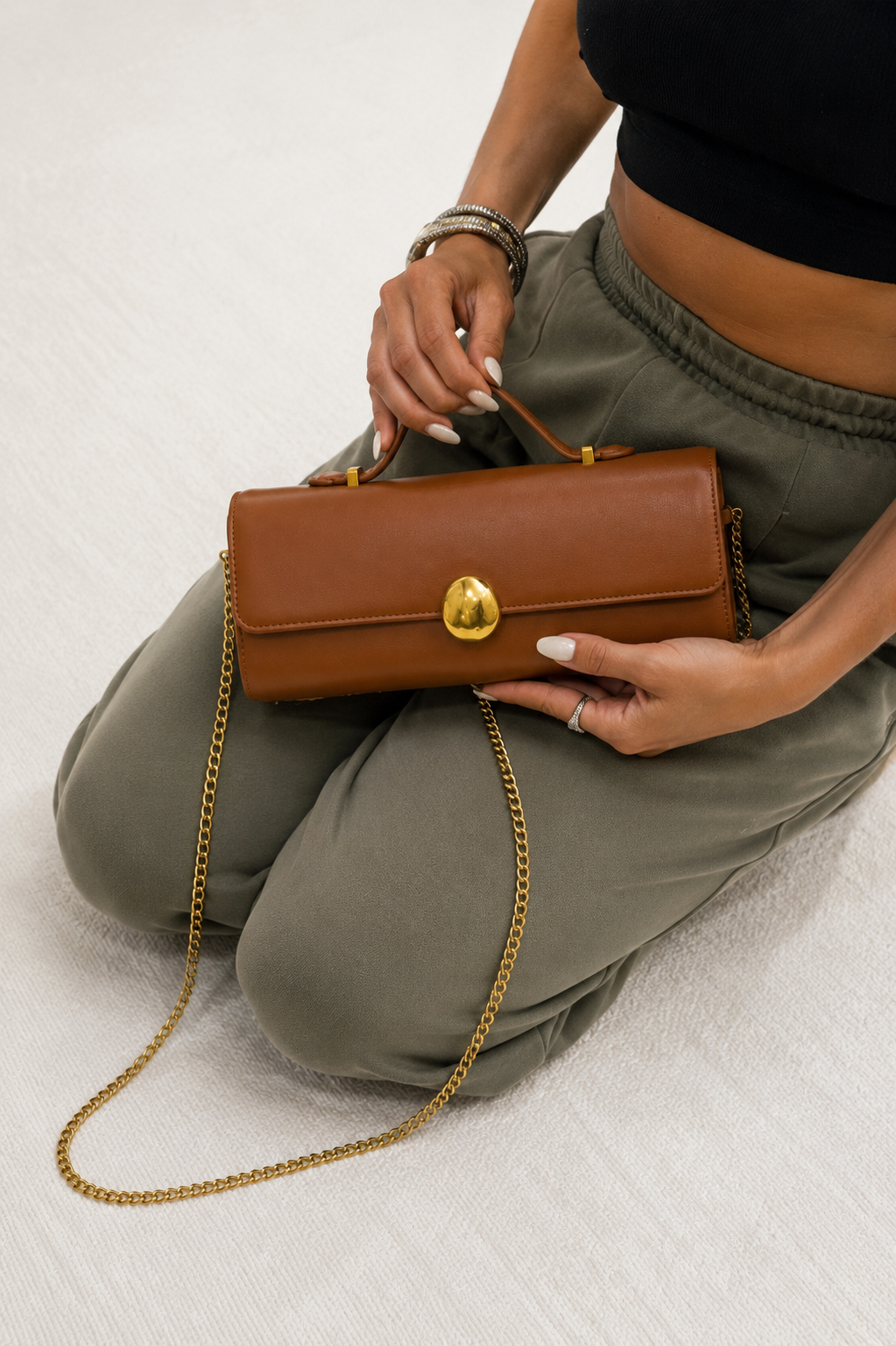 Person holding a brown handbag with a gold chain on a light background. Tan Top Handle Clutch Bag.