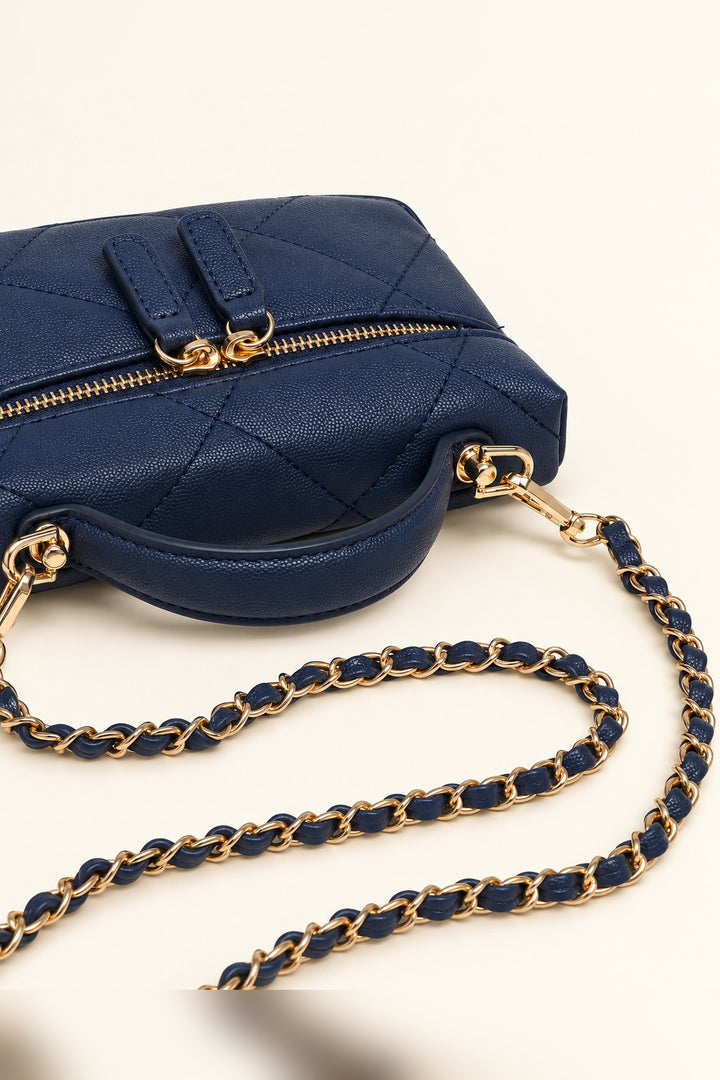 Close detail of the diamond quilting and elongated gold zip pulls on the navy crossbody