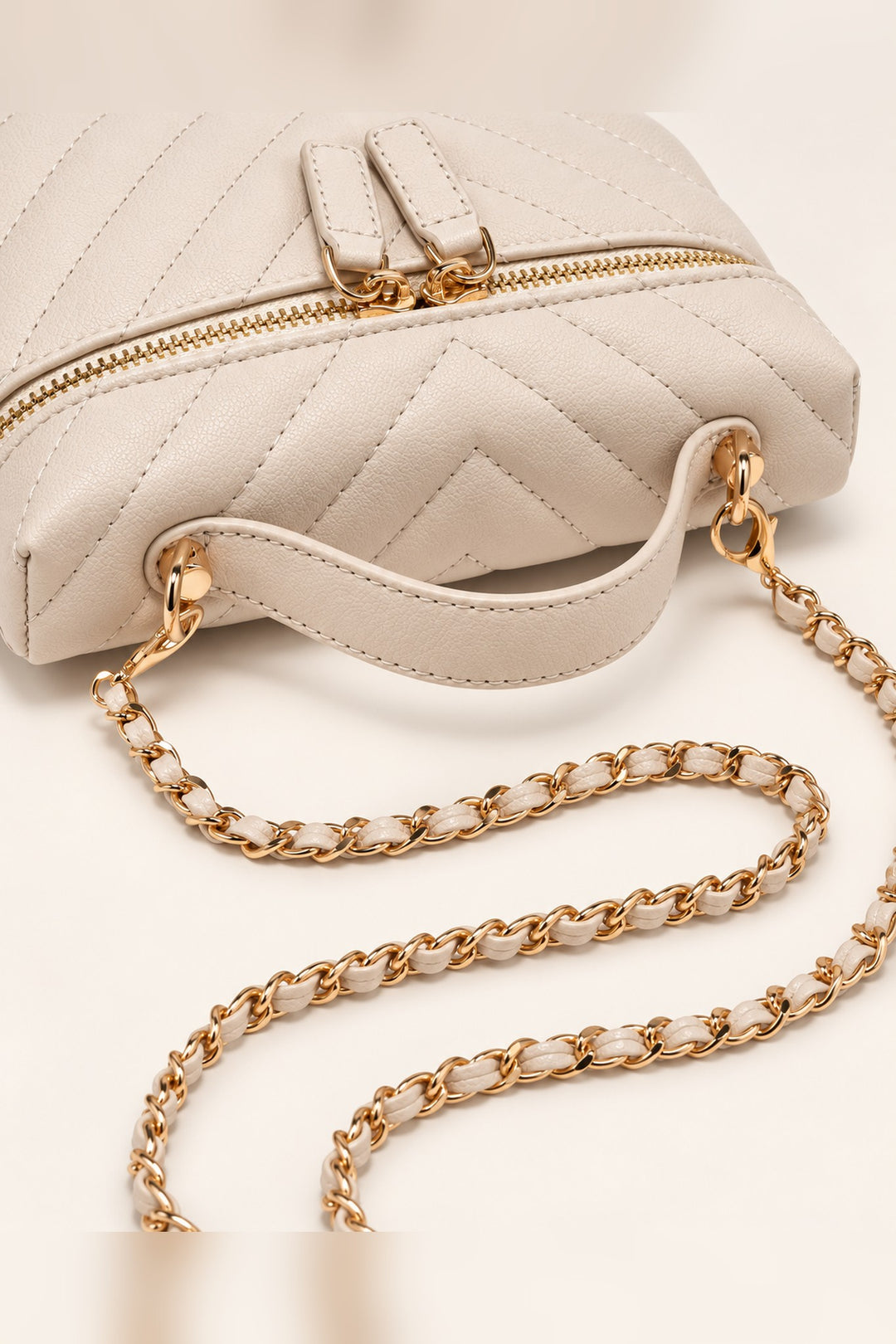 Close detail of the chevron quilting and gold dual zip pulls on the ivory Sella crossbody