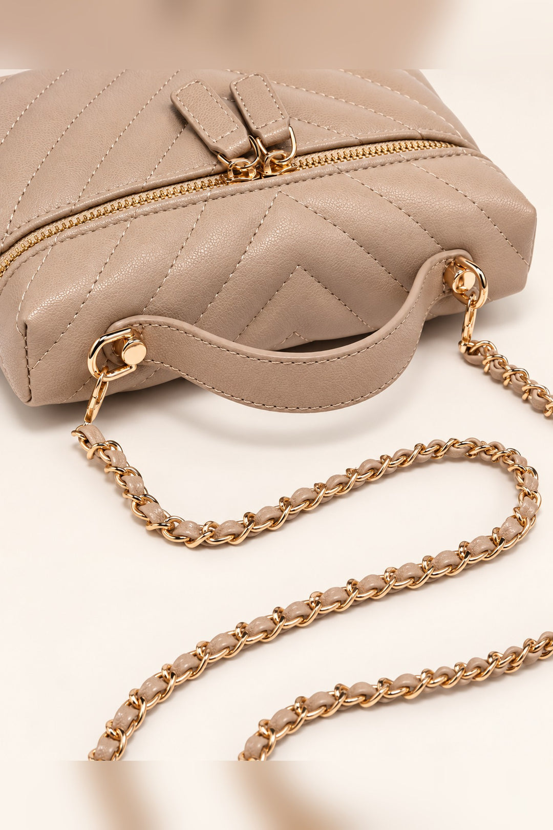 Close detail of the chevron quilting and gold dual zip pulls on the beige Sella crossbody