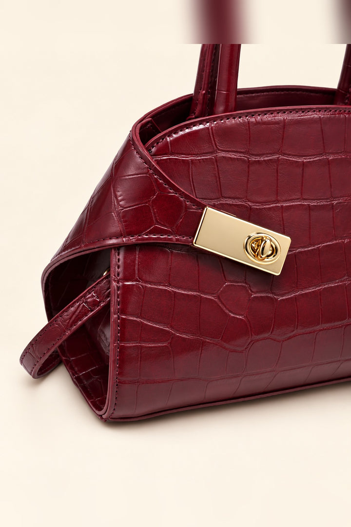 Close detail of the croc texture and gold turn-lock on the burgundy Fable crossbody