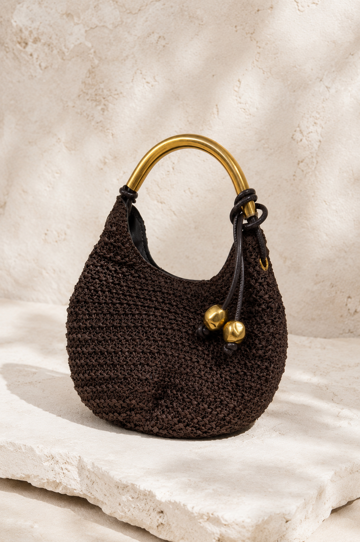 Brown crocheted handbag with gold handle and accents on a textured beige surface. Gold Handle Brown Woven Mini Bag.