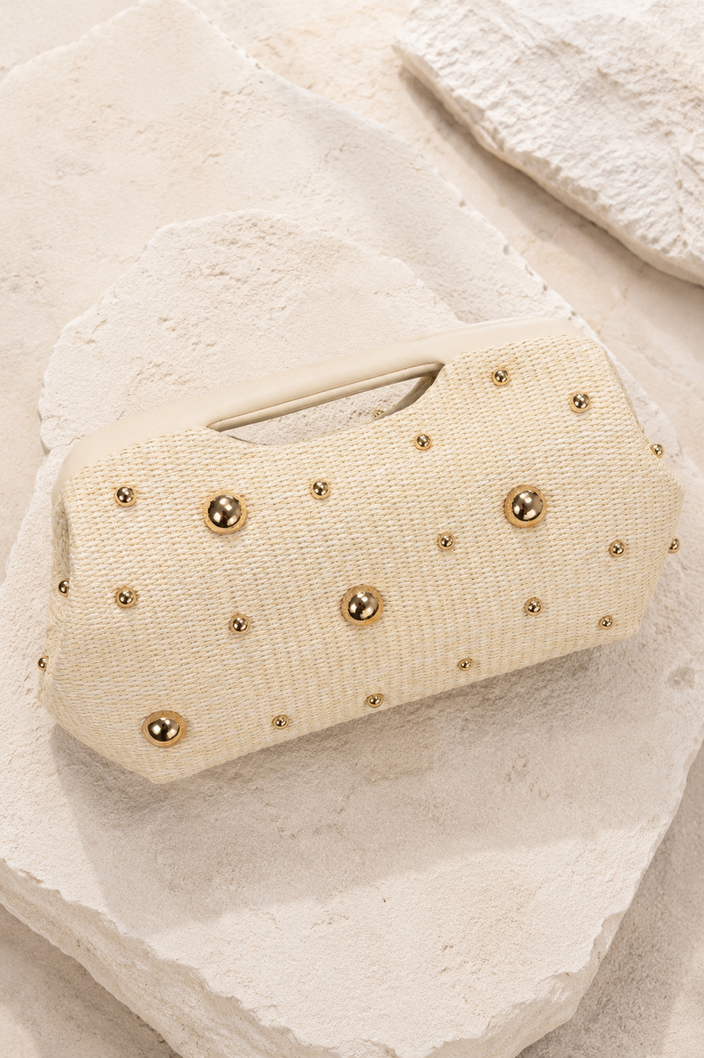 Beige clutch bag with gold studs on a textured beige surface. Ivory Gold Circle Studded Clutch Bag. 