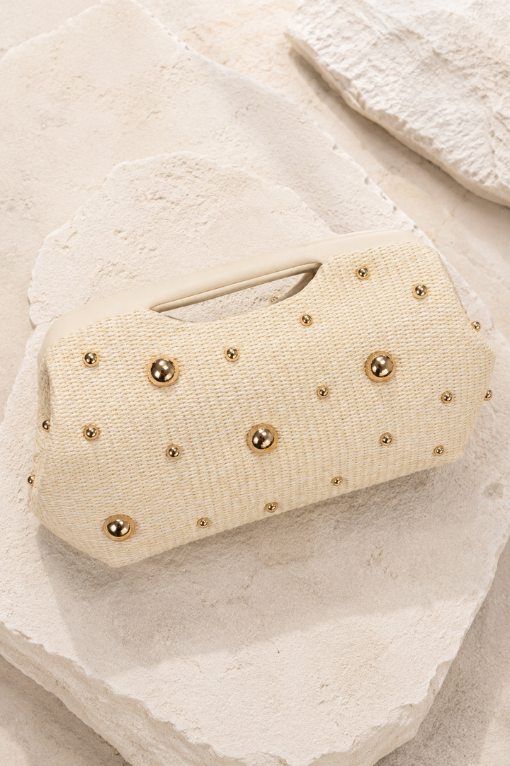 Beige clutch bag with gold studs on a textured beige surface. Ivory Gold Circle Studded Clutch Bag. 