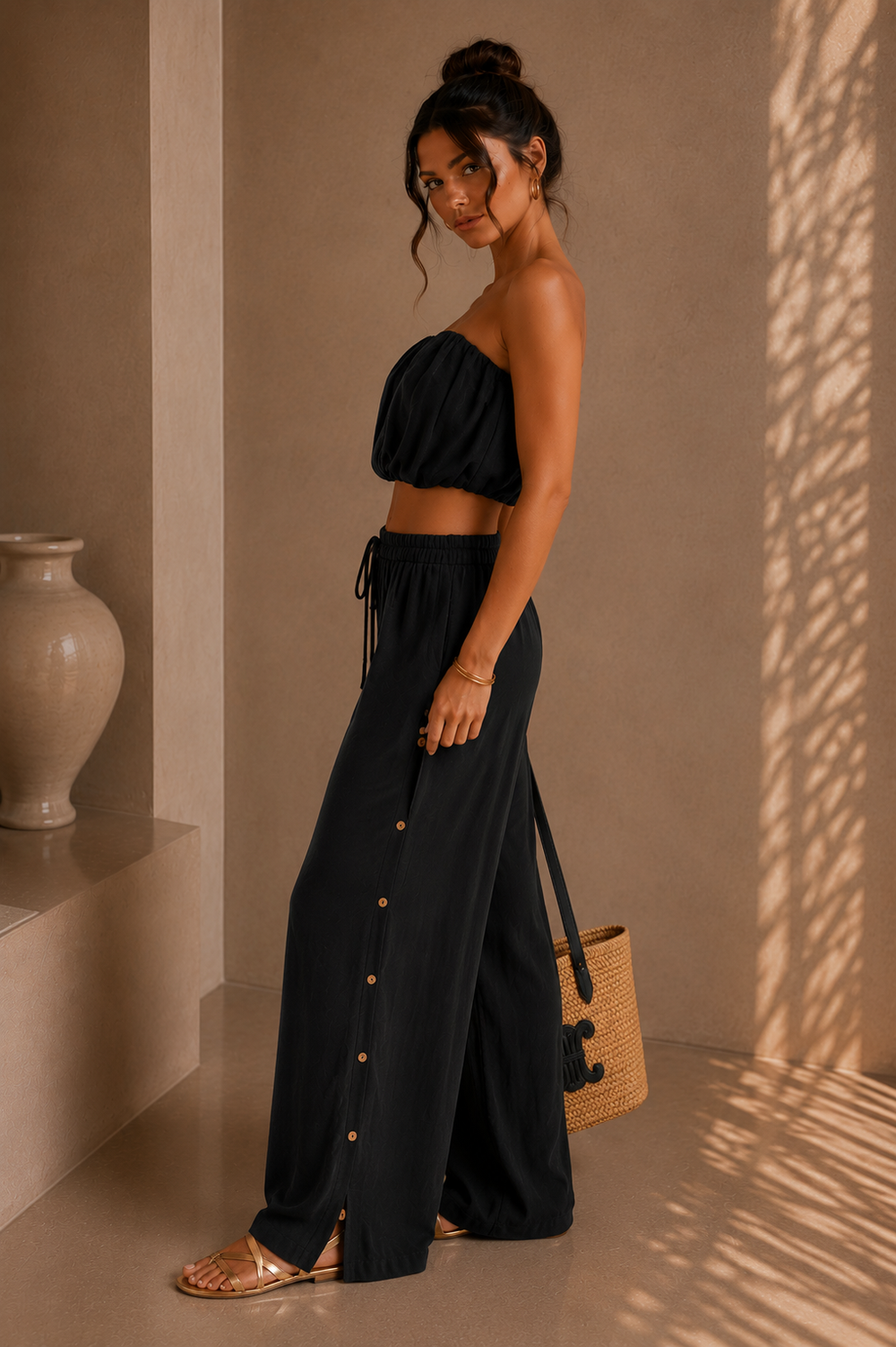 Woman wearing a black outfit with a textured wall and vase in the background. Black Strapless Top & Pants Set.