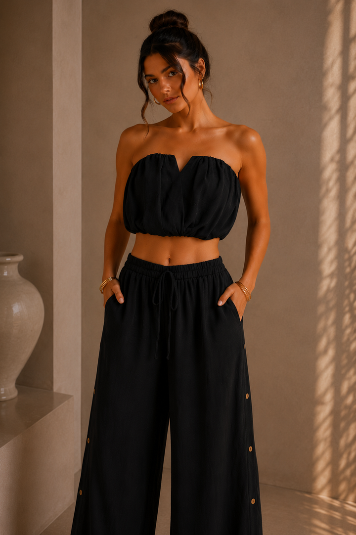Woman wearing a black strapless top and wide-leg pants against a beige wall. Black Strapless Top &amp; Pants Set.