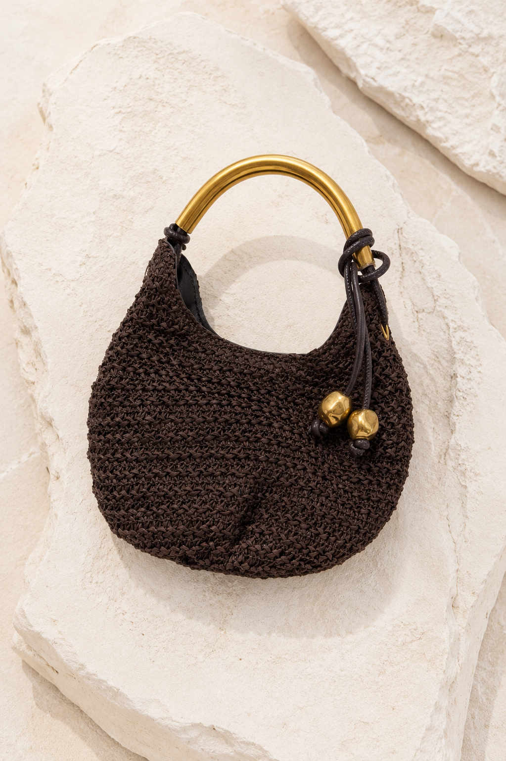 Brown knitted handbag with gold handle and accents on a textured beige surface. Gold Handle Brown Woven Mini Bag.