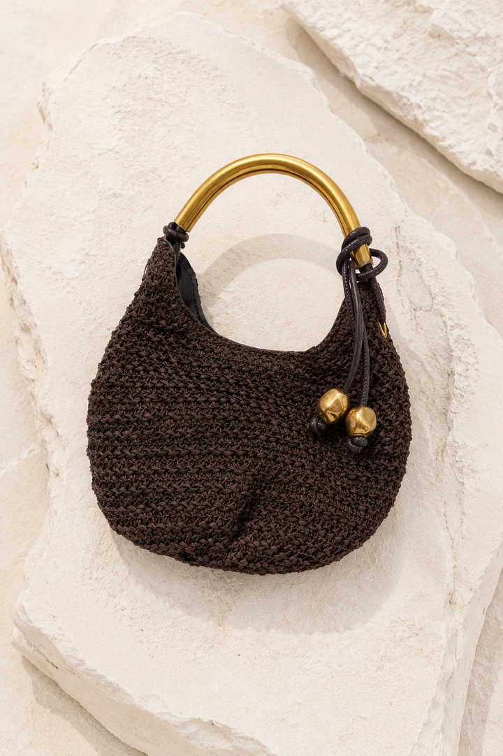 Brown knitted handbag with gold handle and accents on a textured beige surface. Gold Handle Brown Woven Mini Bag.