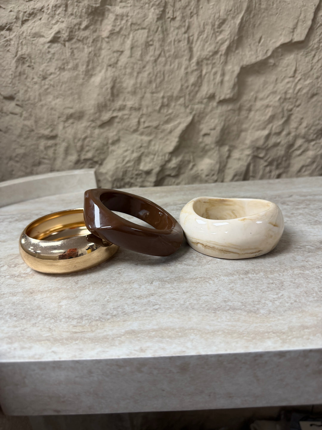 Three ceramic bowls in gold, brown, and beige on a stone surface with a stone wall background. Brown, Ivory & Gold Bangle Set