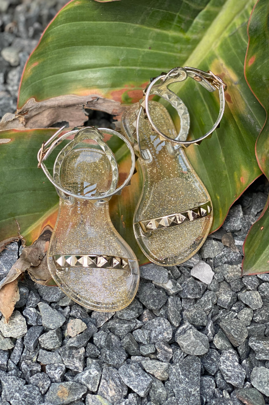 Aria Kids gold jelly sandals with a thin strap across the toes and a thin ankle strap. Shoes for beach and pool days. wear this shoes with a casual chic look