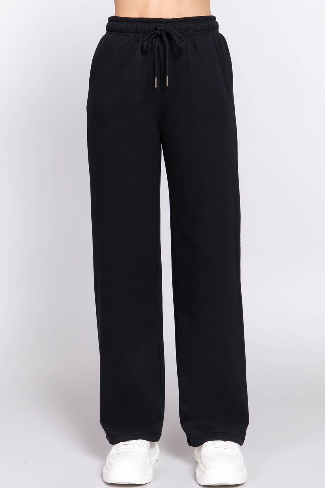 Front view of the black fleece lined straight leg sweatpants with elastic waist and white sneakers