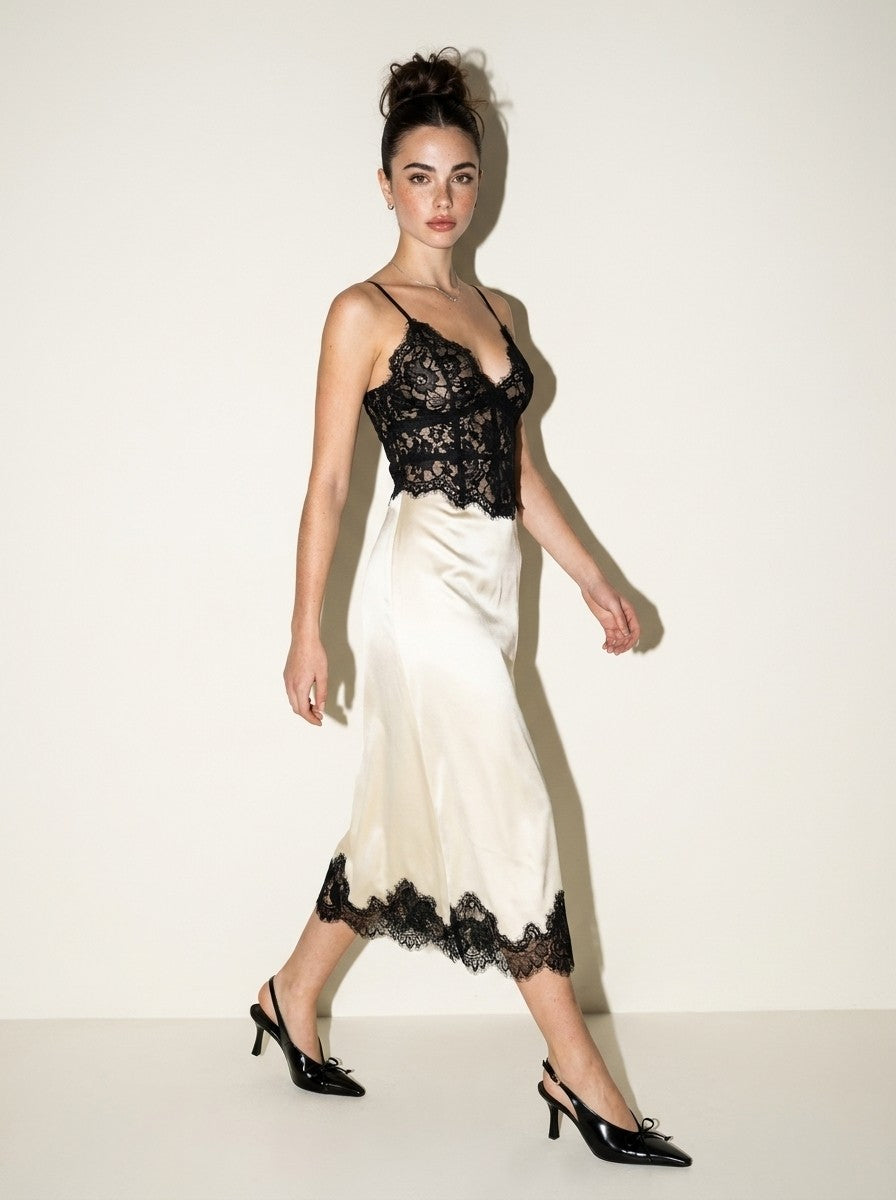 Walking view of the ivory satin midi dress with black lace bodice and scalloped lace hem, black slingback heels
