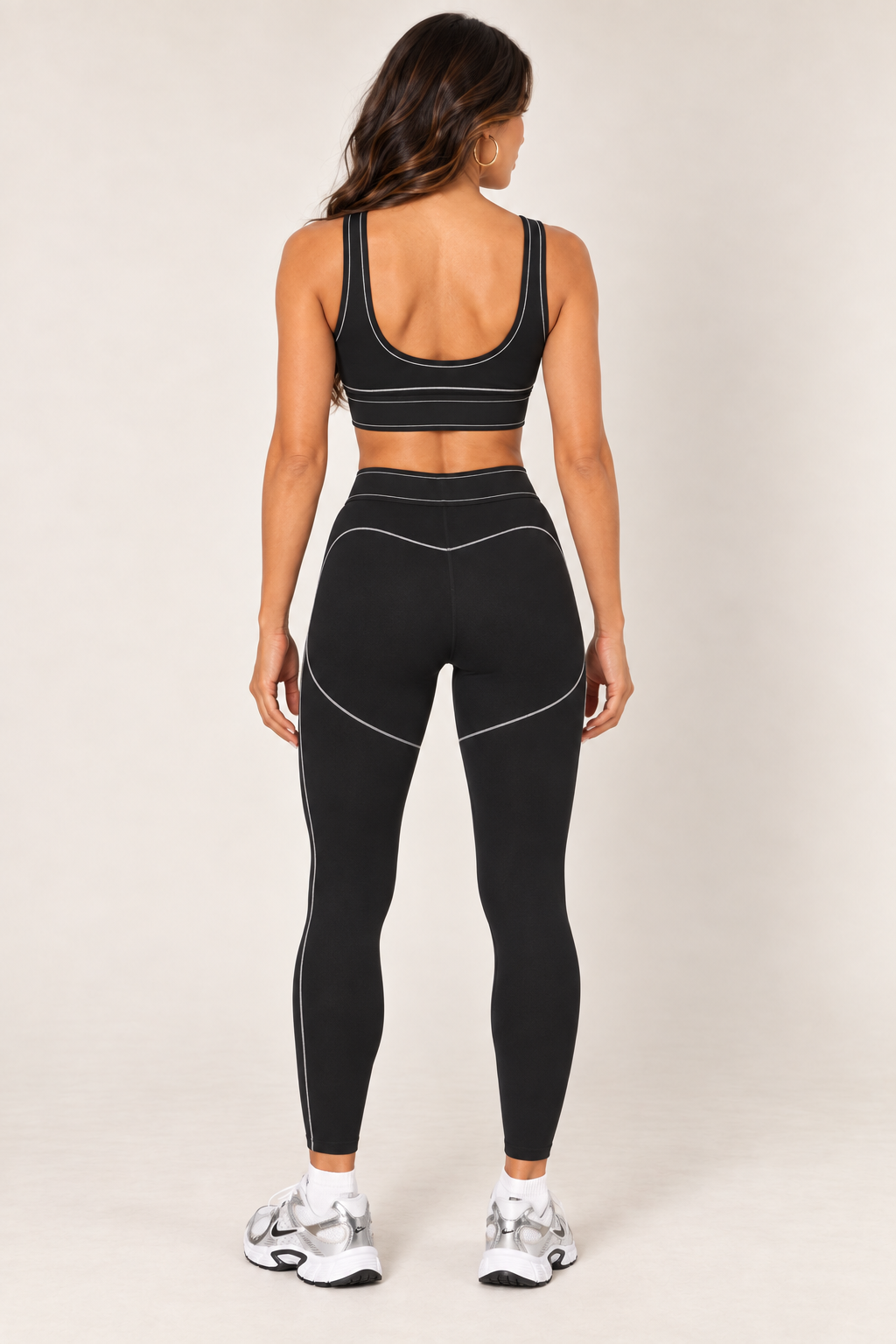 Back view of the black sports bra showing the deep scoop back, wide straps and light contrast stitching, styled with matching black leggings.