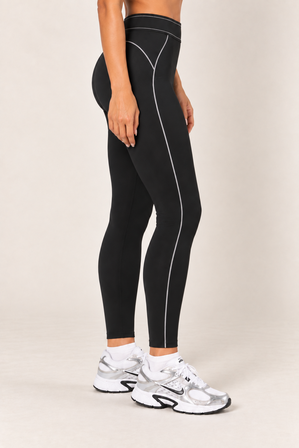 Waist-down side view of black contour leggings highlighting the curved hip seam and light stitching extending down to the ankle-length hem.