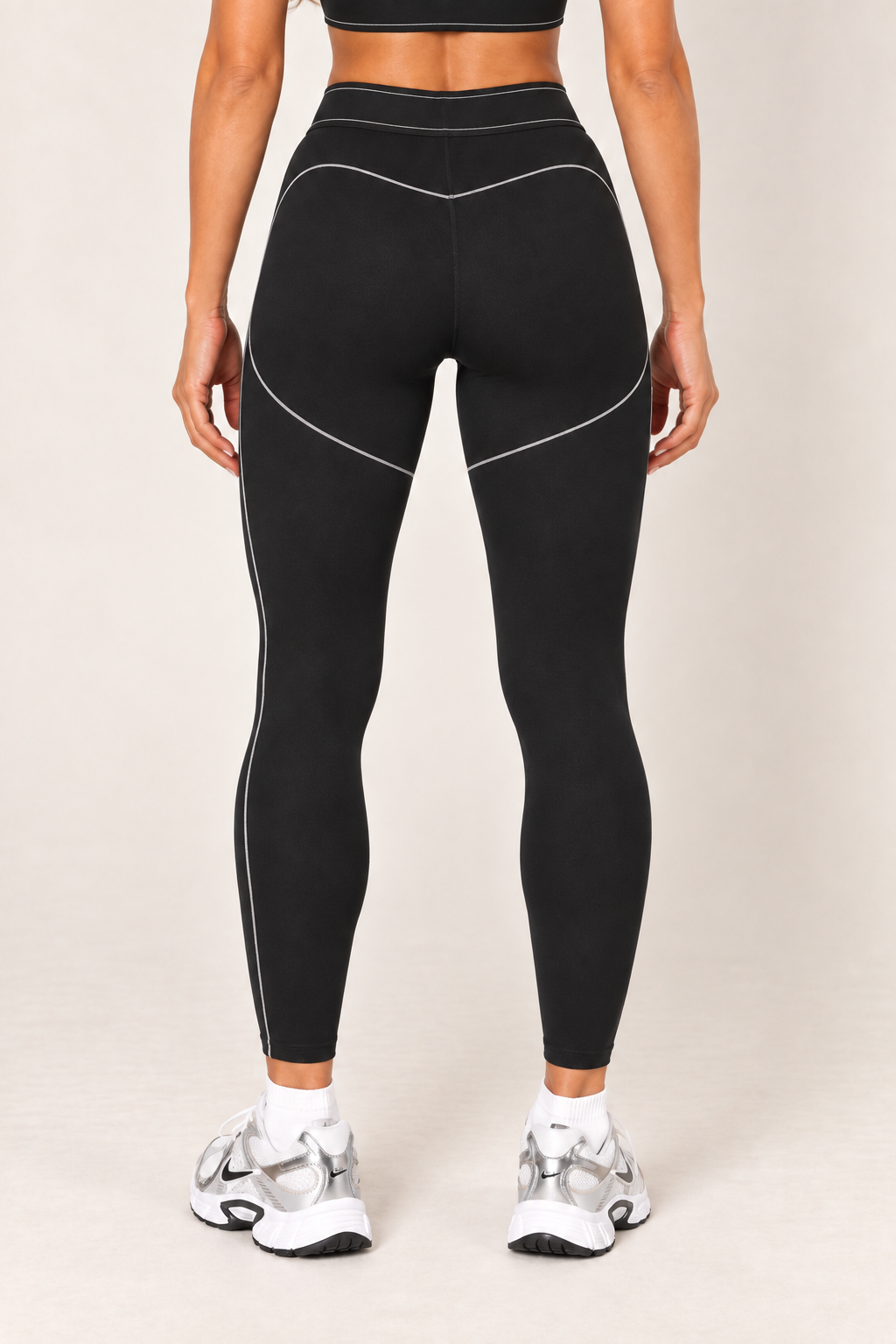 Waist-down back view of black high-rise contour leggings showing the contrast-stitched waistband, curved rear seams and fitted ankle-length silhouette.