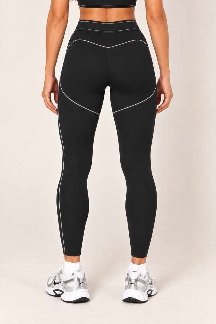 Waist-down back view of black high-rise contour leggings showing the contrast-stitched waistband, curved rear seams and fitted ankle-length silhouette.