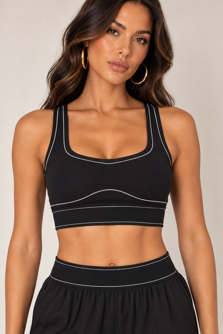 Front close-up of Glowie black sports bra showing wide straps, a shaped neckline, curved underbust seam and pale contrast stitching.