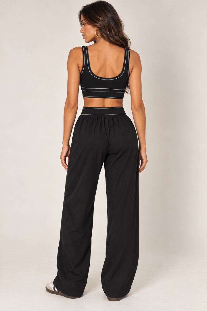 Back outfit view of Glowie black sports bra showing its scoop neckline and contrast stitching, paired with wide-leg pants sold separately.