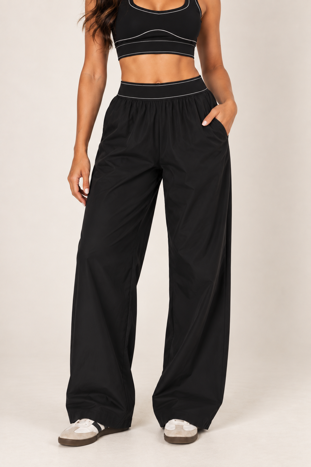 Front close-up of Glowie black nylon pants showing the wide elastic waistband, pale topstitching, gathered fabric and relaxed full-length legs.